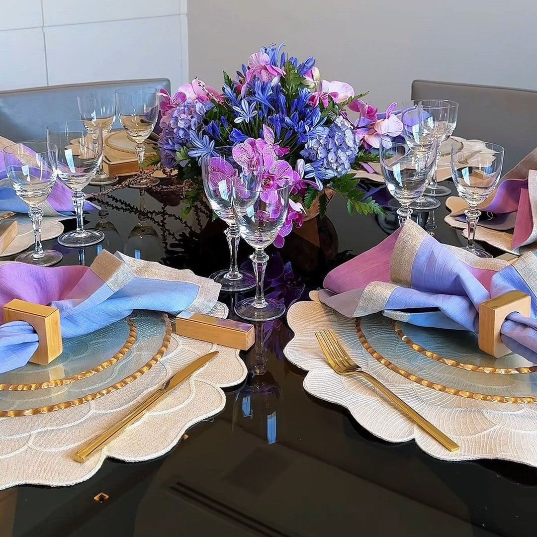 Mesa posta lilás com guardanapos lilás e azul, taças de cristal e arranjo de flores roxas